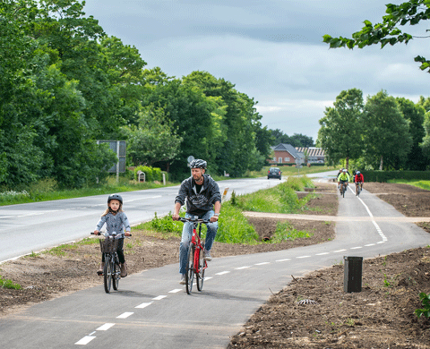 Far og datter cykler sammen på cykelstien langs Hovedvej A1. 