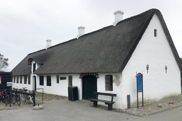 Foto af et traditionelt længehus på Mandø. De traditionelle længehuse på Mandø er smalle og lange, stald og stue er under samme tag, de er udstyret med en lille og lav arkengaf, enkle skorstene og simpel facadeudsmykning.